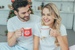 © LIGHTFIELD STUDIOS - laughing young couple with cups of cocoa sitting in bed at home on christmas