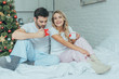 © LIGHTFIELD STUDIOS - happy young couple with cups of cocoa sitting in bed at home on christmas