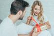© LIGHTFIELD STUDIOS - handsome young man presenting gift to girlfriend in bed at home