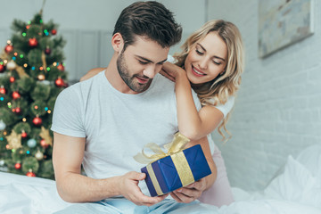 beautiful young woman presenting christmas gift to boyfriend in bed at home