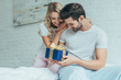 © LIGHTFIELD STUDIOS - beautiful young woman presenting gift to boyfriend in bed at home