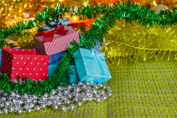 Colorful small gift boxes with gifts among Christmas tinsel and shiny toys and decorations. Winter and holiday scenery by the light of candles.