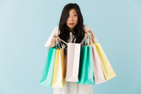 Fototapeta Mapy - Asian young shocked emotional woman isolated over blue background holding shopping bags.