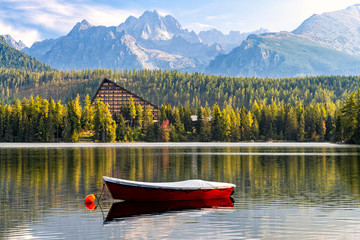 Wall Mural - Peaceful mountain scene with mountain hotel next to a lake with boat. Scenic view of Strbske Pleso, High Tatras National Park, Slovakia. Focus on a boat in front.