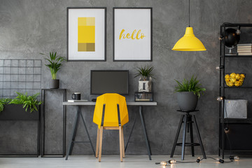 Stylish yellow and grey home office with industrial furniture and urban jungle, real photo with posters on concrete wall