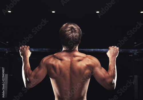 Fotografie, Obraz Rear view of muscular man doing pull up exercise on horizontal bar