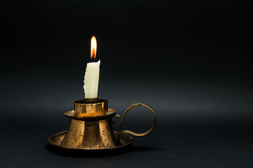 Vintage candle holder with lighted candle isolated in black background