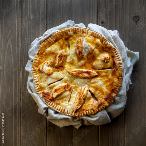 Fényképezés  Apple pie decorated with dough leaves on green dishcloth over wooden table, view