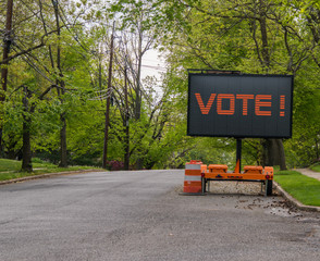 Electric LED sign on trailer that says vote on a suburban street lined with trees