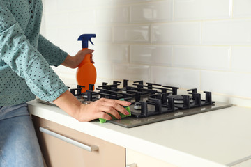 Poster - Woman cleaning gas stove with sponge in kitchen, closeup