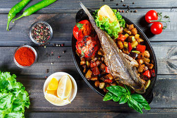 Wall Mural - Baked dorado fish with vegetables and lemon on pan on wooden background close up. Delicious dish of seafood. Top view.