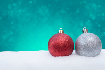 RED AND SILVER CHRISTMAS BALLS ON WHITE SNOW WITH GREEN BOKEH OF LIGTH IN BACKGROUND