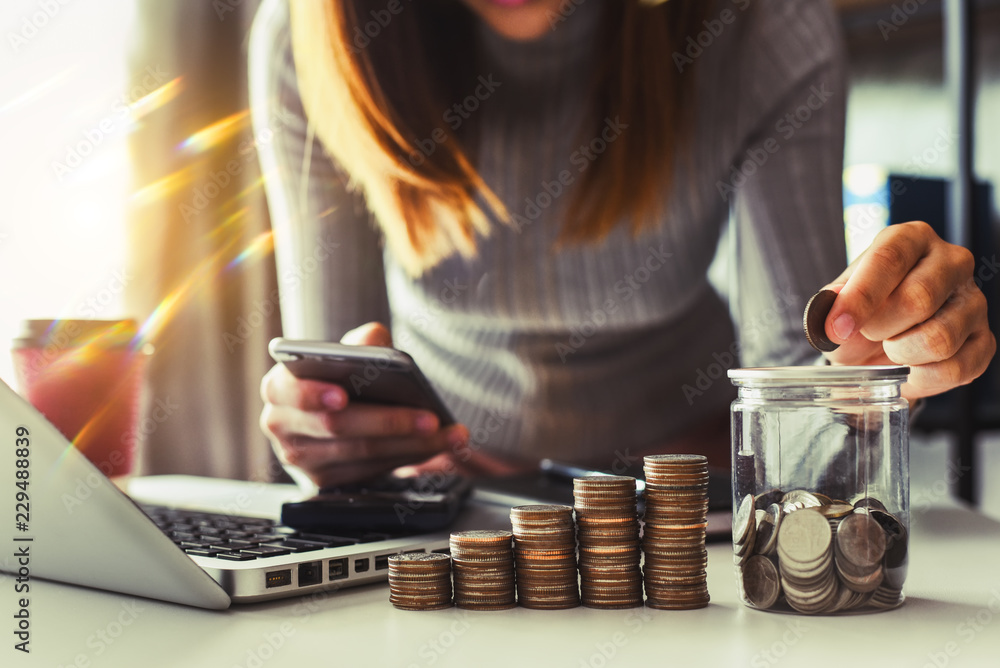 businesswoman holding coins putting in glass with using smartphone and calculator to calculate  concept saving money for finance accounting - obrazy, fototapety, plakaty 