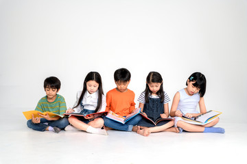 a group of Cute little asian boy and girl reading book while sitting or lying over white background