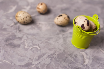 Wall Mural - One green metal bucket with handle full of spotted fresh quail eggs near three eggs on old broken worn gray cement floor with copy space