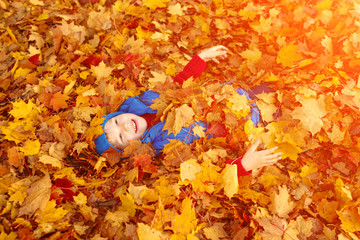 Child in autumn park. Happy adorable boy with fall leaves. The concept of childhood, family and kid laughs outdoors. 
