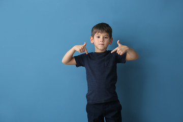 Cute little boy pointing at his t-shirt on color background