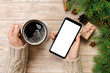 © sosiukin - Female holding cup coffee and smartphone on wooden table with christmas decorations