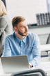 © LIGHTFIELD STUDIOS - handsome young businessman using laptop and looking away in office