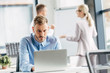 © LIGHTFIELD STUDIOS - concentrated young businessman using laptop and colleagues working behind in office