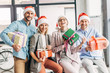 © LIGHTFIELD STUDIOS - happy coworkers in santa hats holding presents and smiling at camera in office