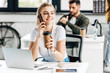 © LIGHTFIELD STUDIOS - attractive young woman talking by phone and drinking coffee at office with colleague on background