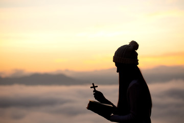 Silhouette off woman hands holding wooden cross on sunrise background, Crucifix, Symbol of Faith.