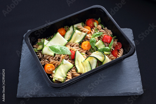 Fototapeta na szkło Dieta pudełkowa. Sałatka makaronu z cukinią i pomidorami podana w naczyniu jednorazowym.