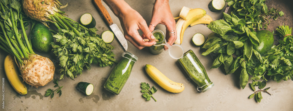 Making green detox smoothie. Flat-lay of ingredients for making smoothie and female hands holding bottle with straw over concrete background, top view. Weight loss, healthy food concept - obrazy, fototapety, plakaty 