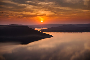 Scenic landscape view of beautiful orange sunset over the horizon and calm lake. Two islands. Sky reflection in the water