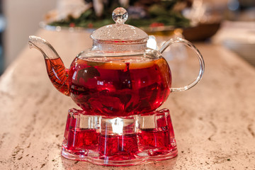 Glass teapot with red fruit tea on a stand