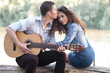 © soleg - young couple sitting on a log by the river and playing guitar, summer nature, bright sunlight, shadows and green leaves, romantic feelings