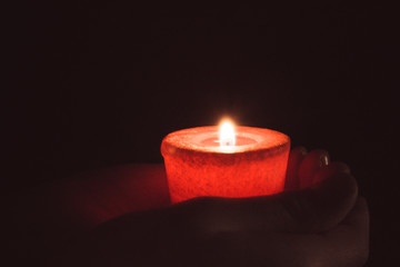 lonely flame burning red candle in hand in the dark