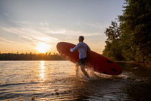 Man With Paddleboard Walking Into Lake During Sunset