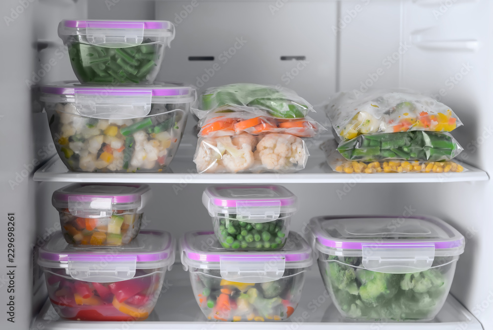 Containers and plastic bags with frozen vegetables in refrigerator