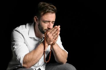 Religious young man praying to God on black background