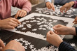 © Pixel-Shot - Group of people assembling puzzle on dark table