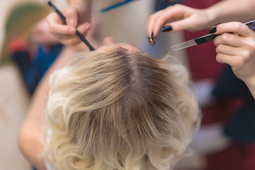 Wall Mural - The work of a professional makeup artist - hairdresser, makes the hair style of a beautiful blonde girl.