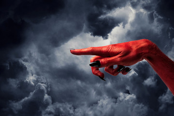 Halloween red devil monster hand with black fingernails against a dark sky