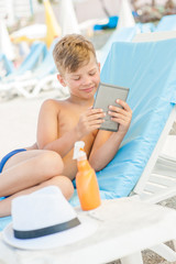 Wall Mural - Young boy reading on electronic book on summer beach