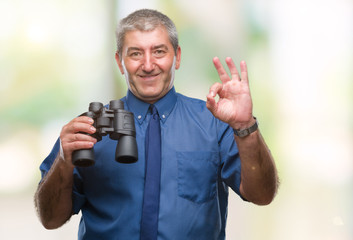 Canvas Print - Handsome senior man looking through binoculars over isolated background doing ok sign with fingers, excellent symbol