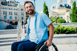 cheerful handsome man in wheelchair looking at camera on street