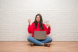 © Krakenimages.com - Young brunette woman sitting on the floor over white brick wall paying holding dollars annoyed and frustrated shouting with anger, crazy and yelling with raised hand, anger concept
