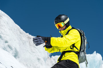 Professional skier in a helmet with a backpack and a ski mask standing on a glacier is preparing to jump wearing membrane gloves. The concept of quality training for the sport