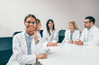 © bnenin - Beautiful smiling female doctor looking at camera while her colleagues are sitting in the background.