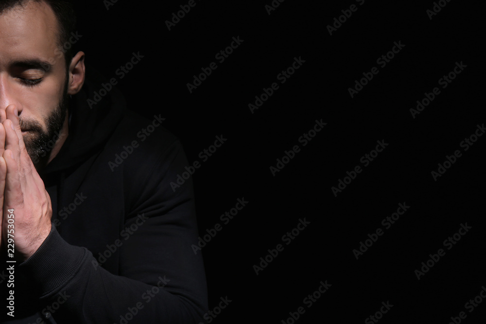 Religious young man praying to God on black background