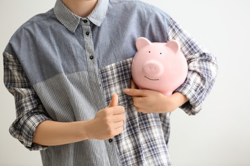 Woman holding piggy bank on light background