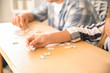 © Pixel-Shot - Young people assembling puzzle on wooden table