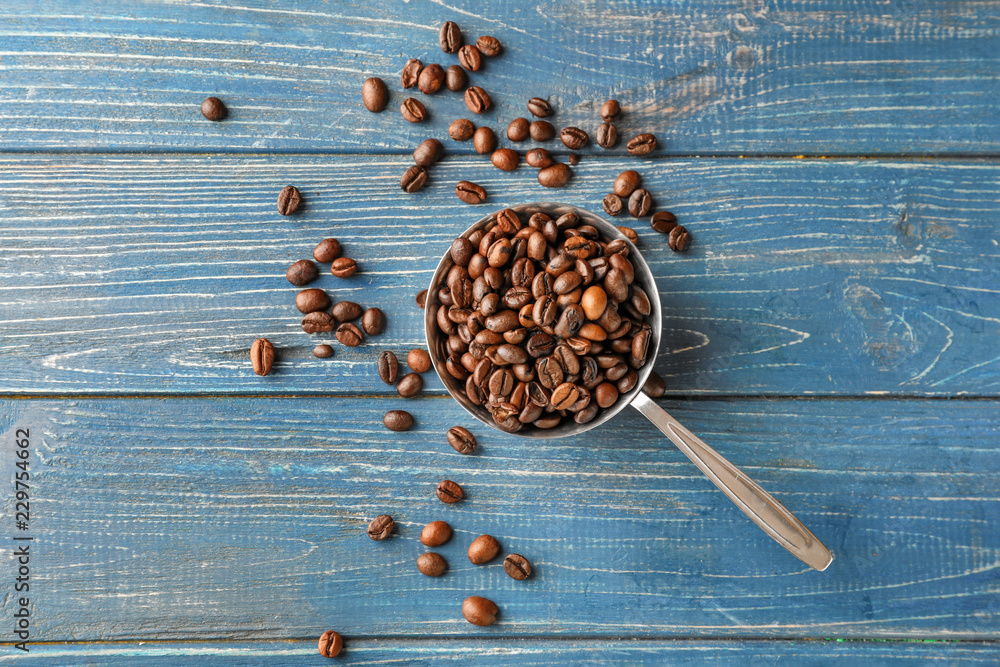 Sauce pot with coffee beans on color wooden background