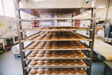 Picture of two male bakers in white uniform pushing together shelves full with fresh baked cookies.